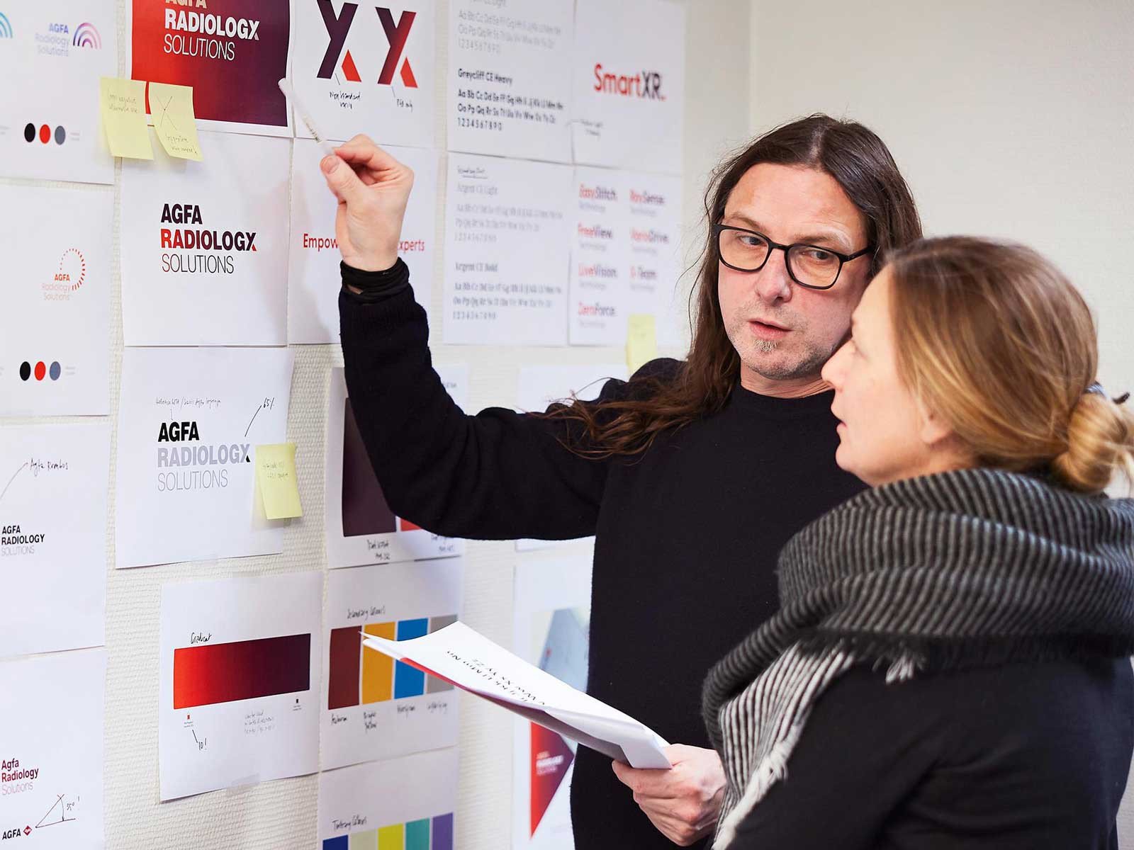 Brandle - Nieuw logo voor AGFA Radiology Solutions Twee personen bespreken branding concepten voor Agfa Radiology Solutions aan een muur vol logo-ontwerpen, kleurstalen en notities.