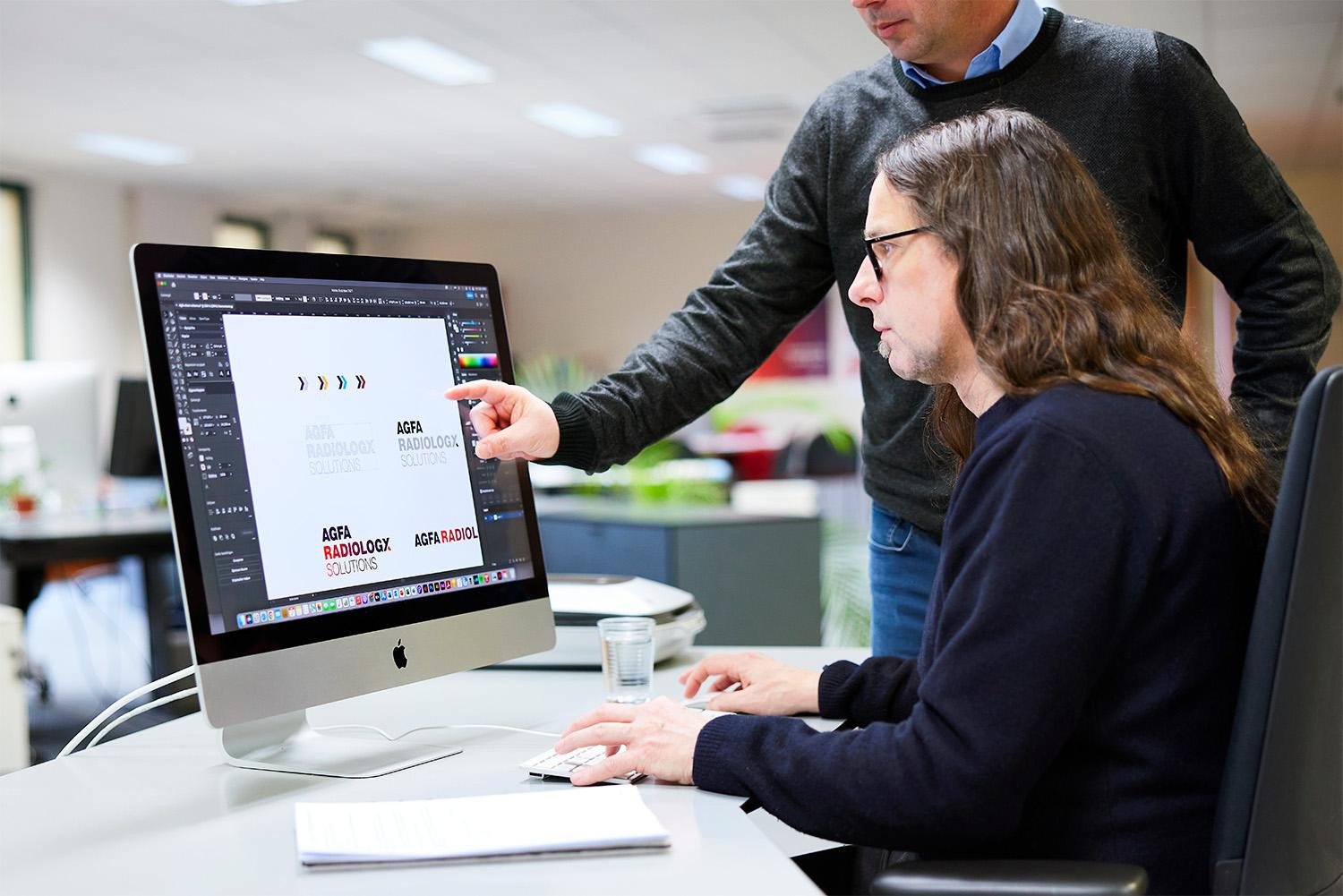 Brandle - Bespreking nieuwe huisstijl voor Agfa Radiology Solutions Designers bespreken logo-ontwerpen voor Agfa Radiology Solutions aan een iMac op kantoor.
