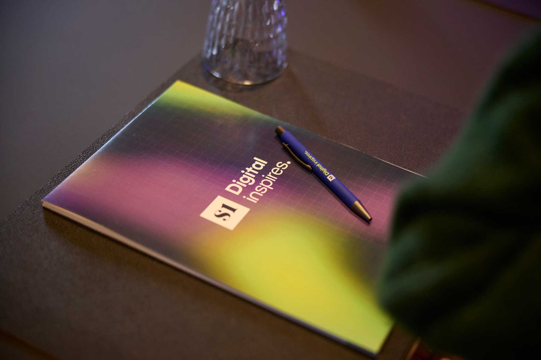 Brandle - Nieuwe huisstijl van S1 Digital op notitieboek en balpen Notitieboek en pen met S1 Inspires-branding op een conferentietafel.