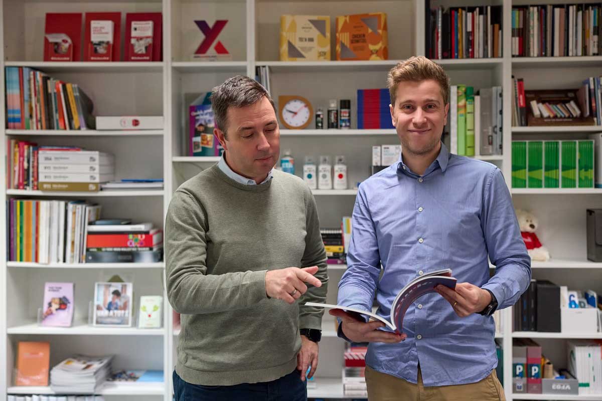 Brandle - Overleg tussen collega\'s Twee collega’s bekijken samen een brochure in een kantooromgeving met boekenkast.